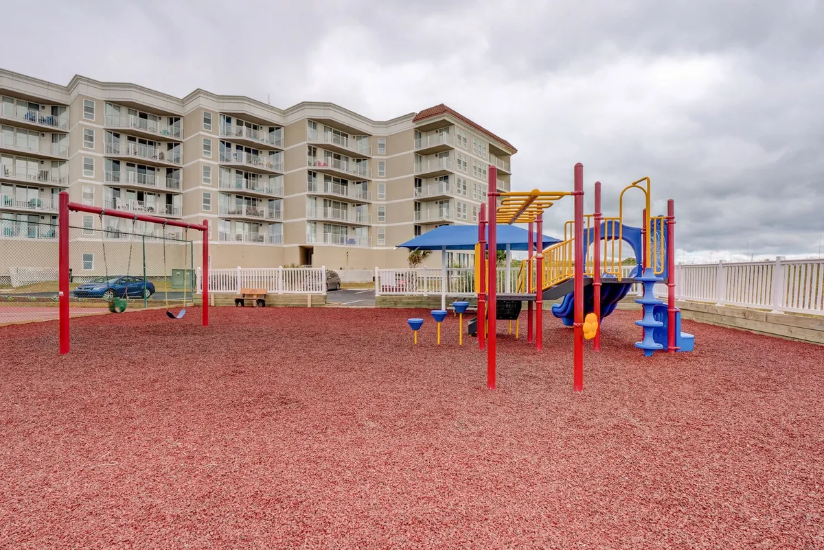 A cheerful outdoor playground features modern equipment, swings, and a sandy play area bustling with children at play. The surrounding area is ideal for family gatherings, picnics, and spontaneous games.