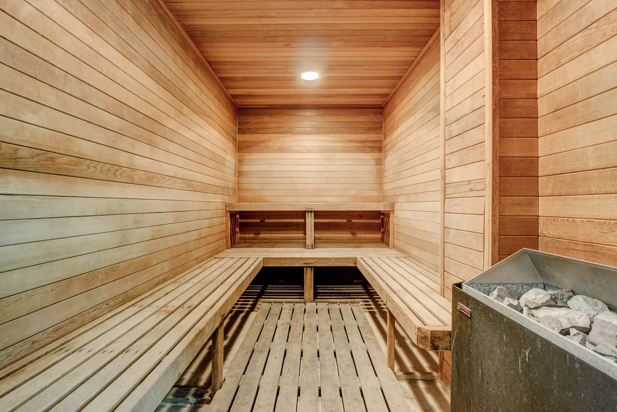 A modern interior sauna with clean wooden benches and walls, centered around a sauna heater. The calming space invites relaxation and wellness.