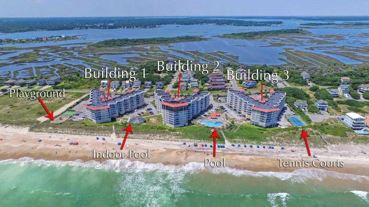 A vibrant exterior view of the resort shows multiple buildings flanking both an indoor and outdoor pool, tennis courts, and a colorful playground. The area is lively and family-friendly, offering multiple recreational options for kids and adults alike.