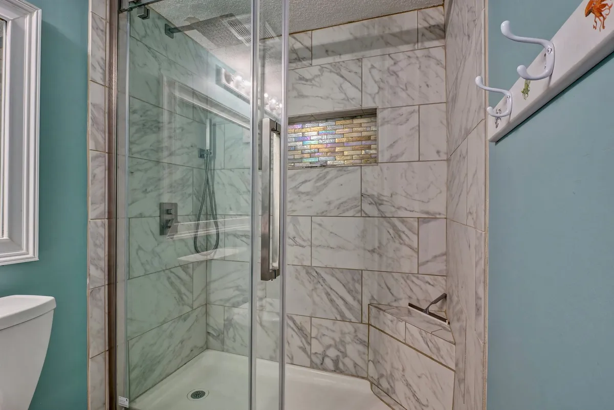 A modern bathroom with a glass shower enclosure, elegant marble tile, and a colorful accent strip, creating a calm and rejuvenating atmosphere ideal for unwinding after a sun-filled day.