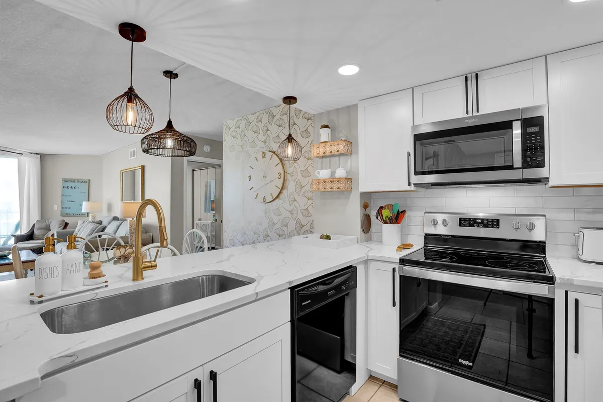 A bright, open kitchen featuring a luxurious marble countertop, stylish pendant lights, and an eye-catching wall clock. The open layout seamlessly connects to the dining and living areas, inviting both cooking and socializing. Upscale appliances are visible and the space feels welcoming and functional, ideal for family gatherings or entertaining guests.